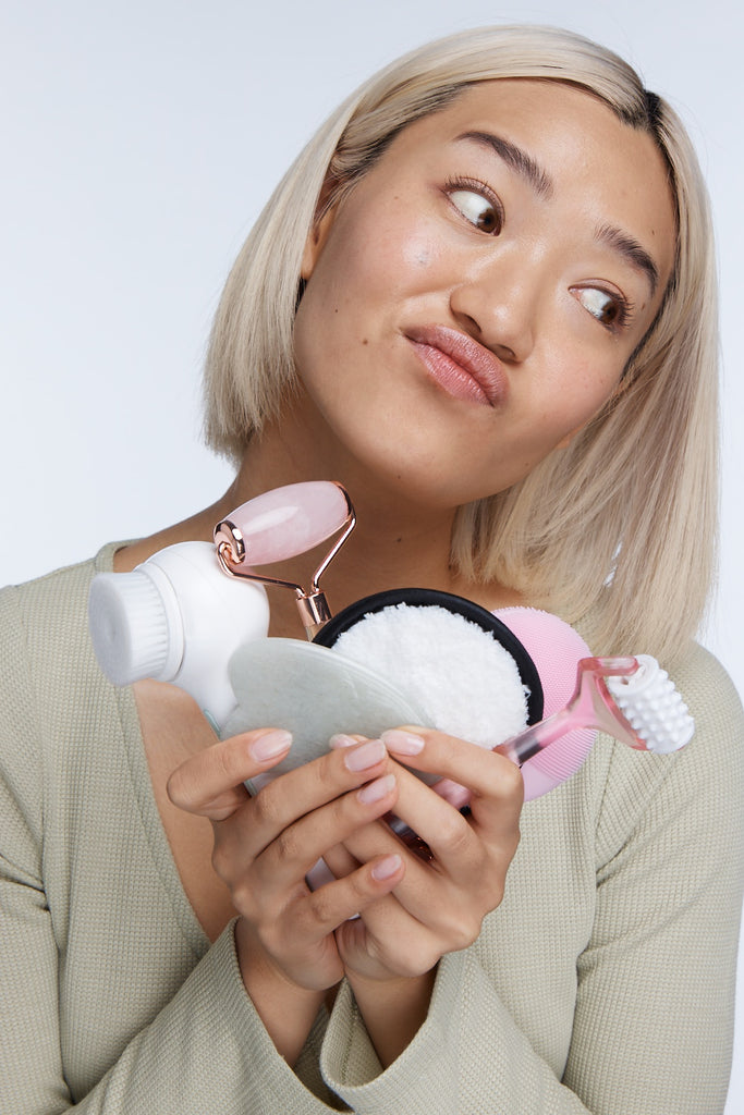 Model holding lots of skincare tools to camera looking unhappy