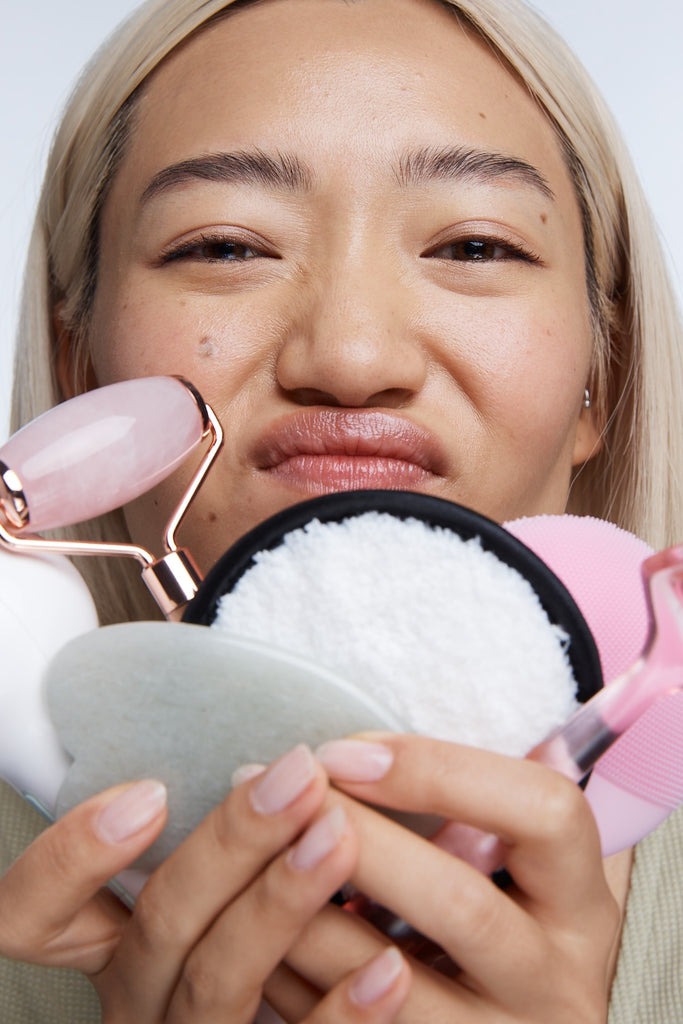 Model holding lots of skincare tools to camera looking unhappy