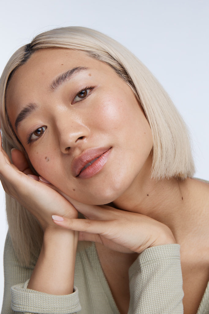Model looking at camera with hands on face and clean glowy skin
