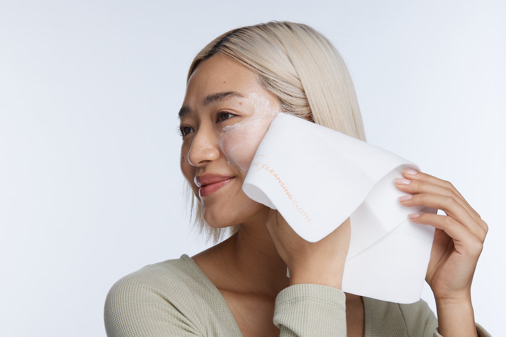 Model smiling wiping cleanser from cheek with cleansing cloth