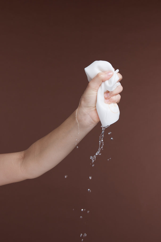 Hand squeezing water from Cleansing Cloth